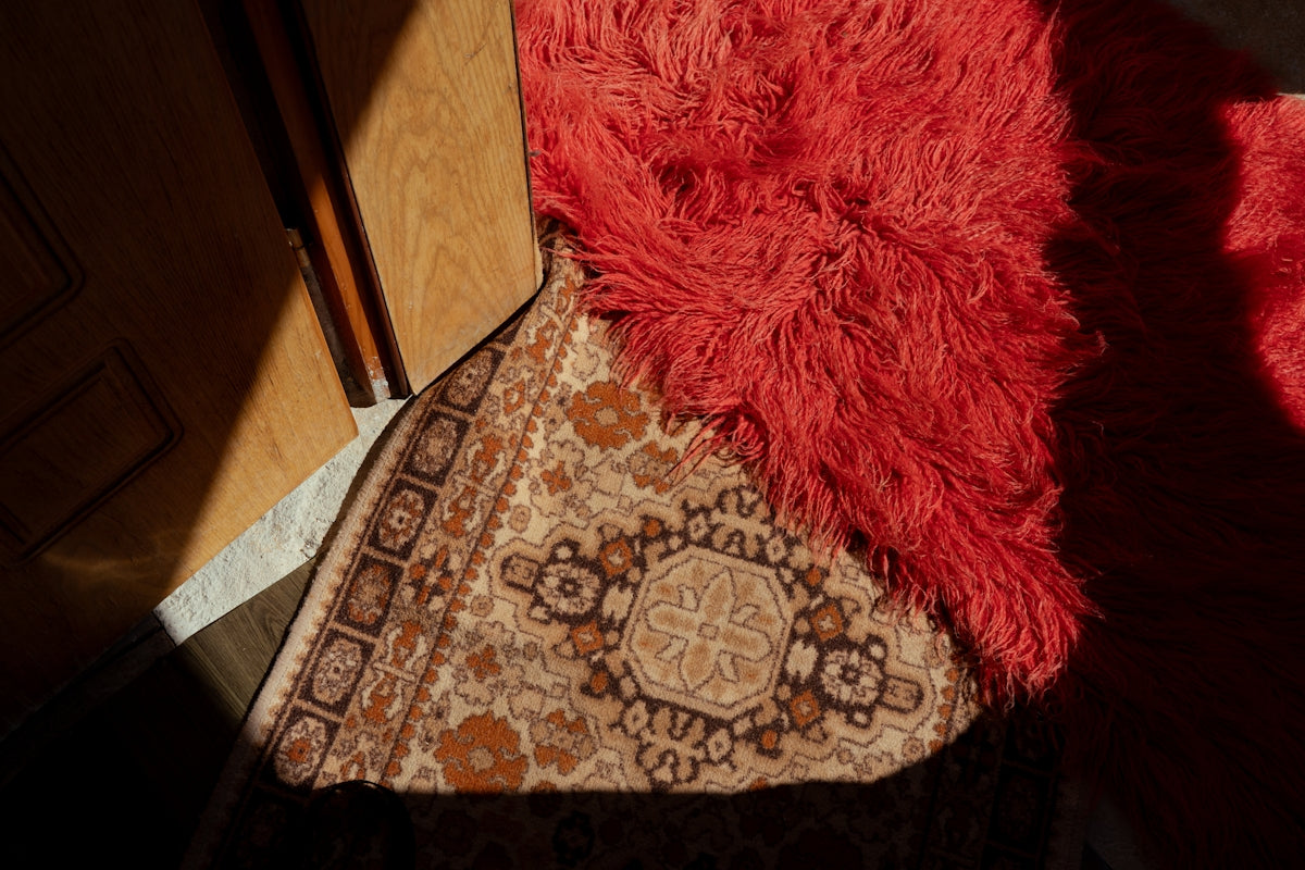 Overlapping red fluffy and patterned beige rugs on a floor