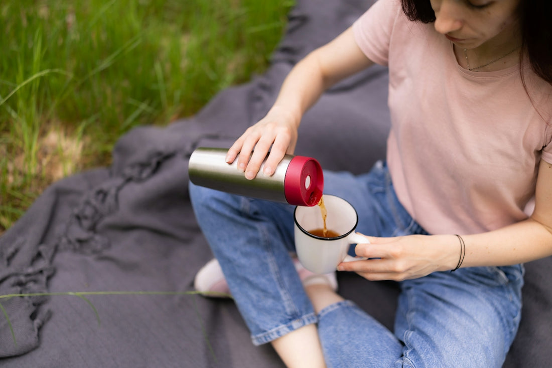 A woman pouring tea from a metal thermos into a white mug outdoors