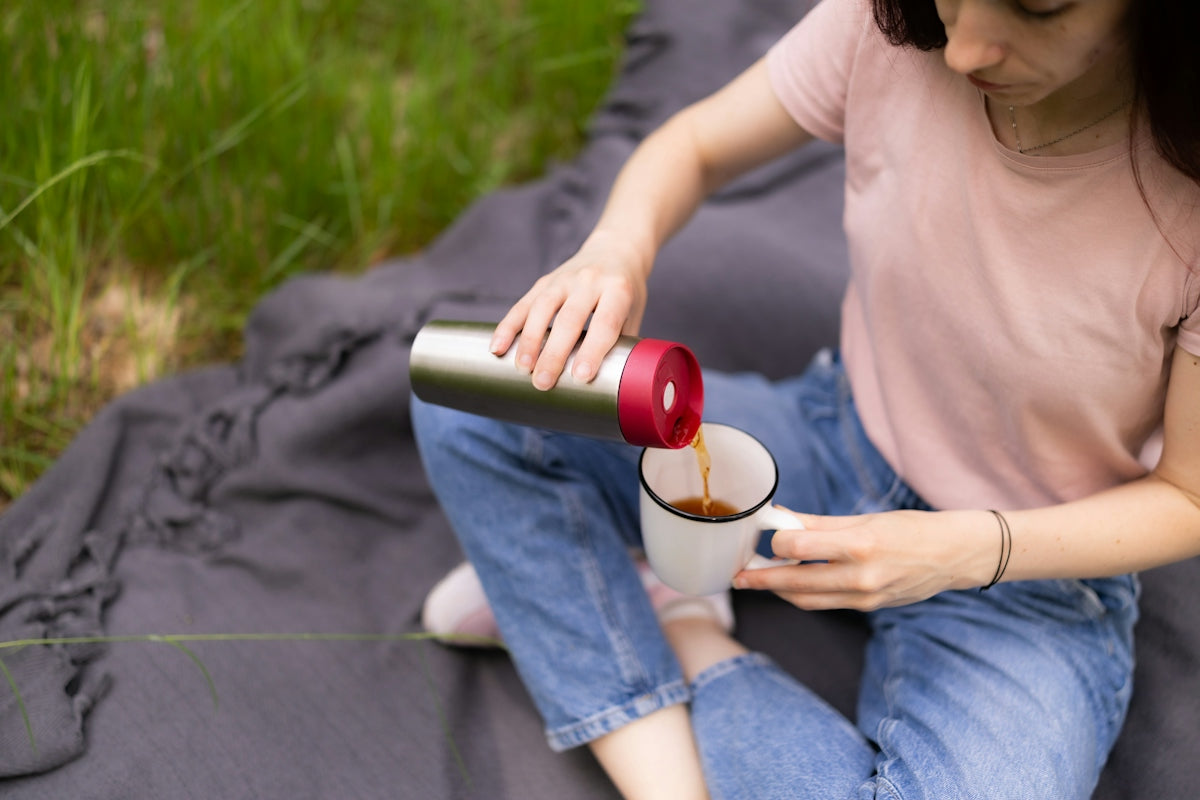 A woman pouring tea from a metal thermos into a white mug outdoors